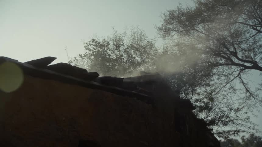 Sunlight streams through smoke rising from the rough tiled roof of a rustic building