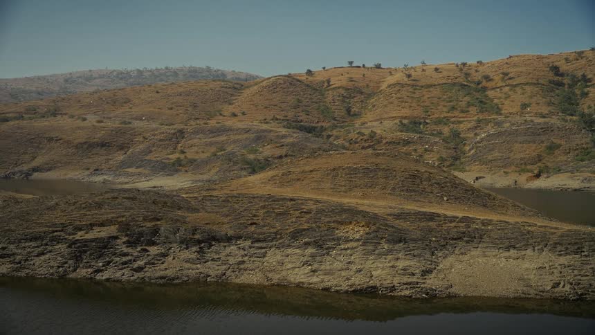 Arid landscape with rocky hills and water body reflecting dry terrain at sunset