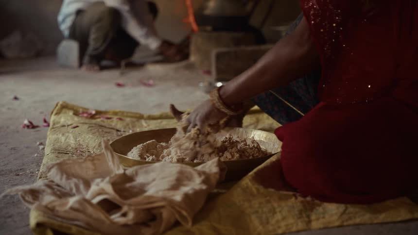 Person kneeling on yellow cloth kneading dough in large bowl in rustic kitchen