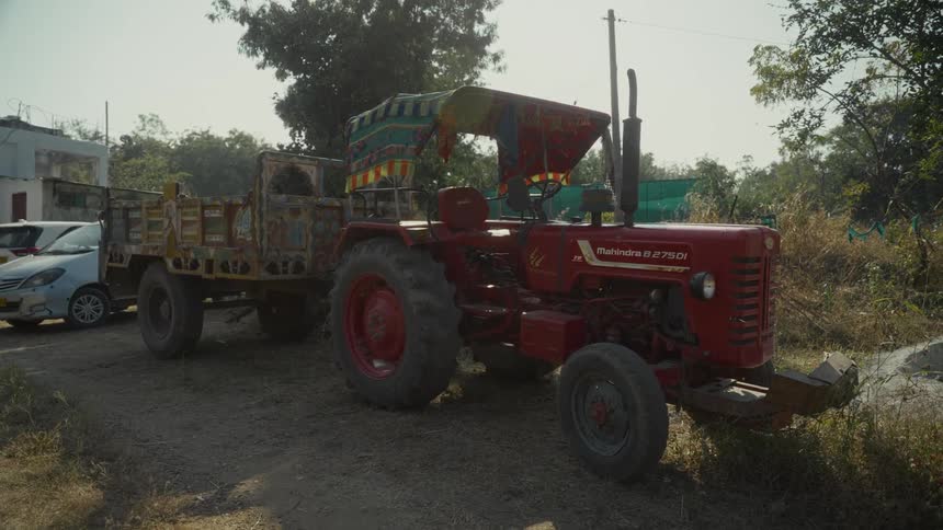 A red tractor with a colorful canopy sits parked on a dirt road hitched to a wooden trailer