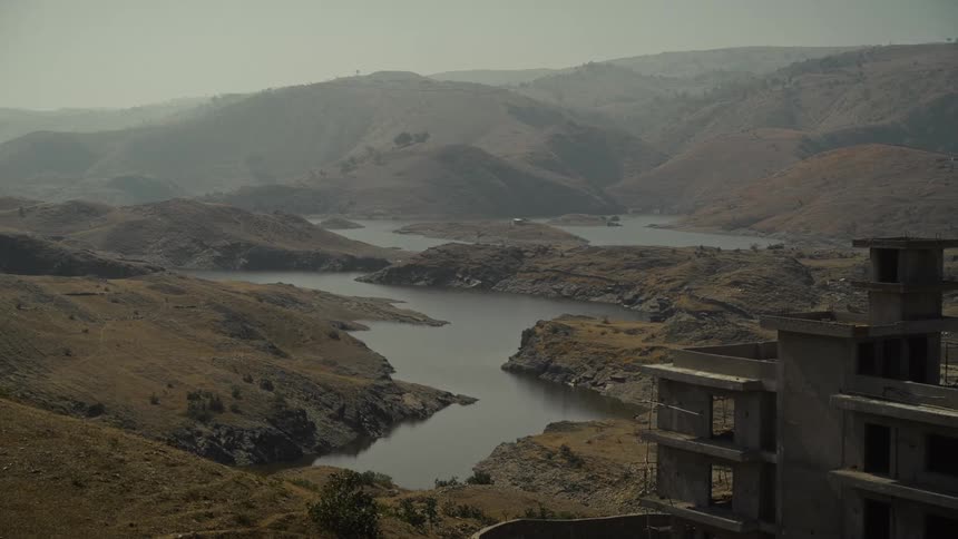 A building under construction stands in a valley on a foggy day beside a stream that winds through and links a series of hills