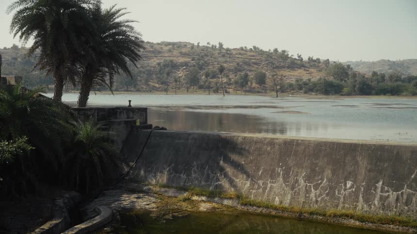 Dam with water flowing surrounded by vegetation and hills in the background