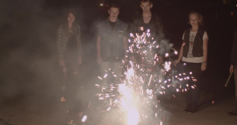 Group of people standing watching small fireworks go off on road