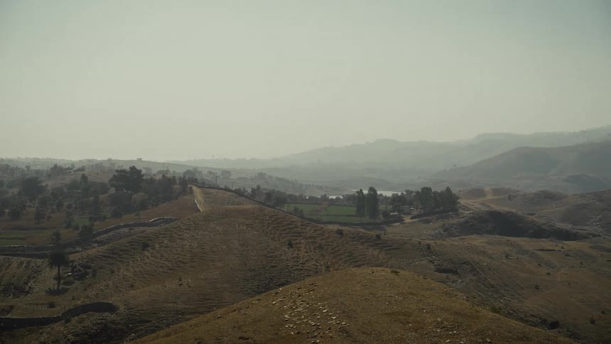 Peaceful landscape with dry hills and winding river reflecting terrain under hazy sky
