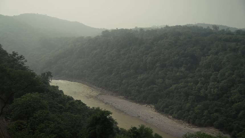 A wide murky river flows through a lush treecovered valley as mist hangs over the distant rolling hills creating a serene and expansive scene