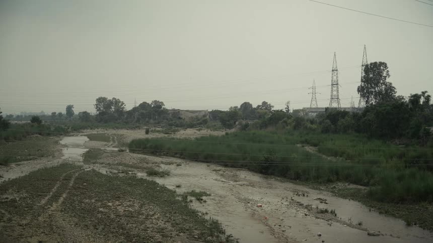 Shallow river winding through rocky terrain with power towers in background under cloudy sky