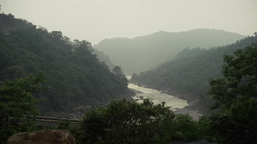 A murky river carves a path through a deep forestcovered valley as distant mountains fade into the thick haze