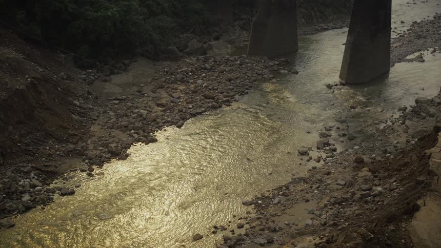 Shallow goldenhued river flowing under concrete bridge in rocky terrain