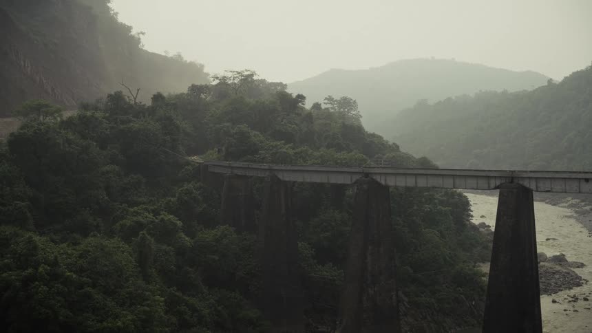Elevated bridge supported by concrete pillars crossing forested valley with winding river at dawn