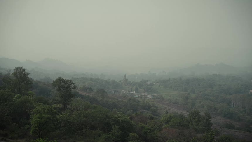 Rural village next to a road surrounded by a forest covered in fog with hills on the background outdoors