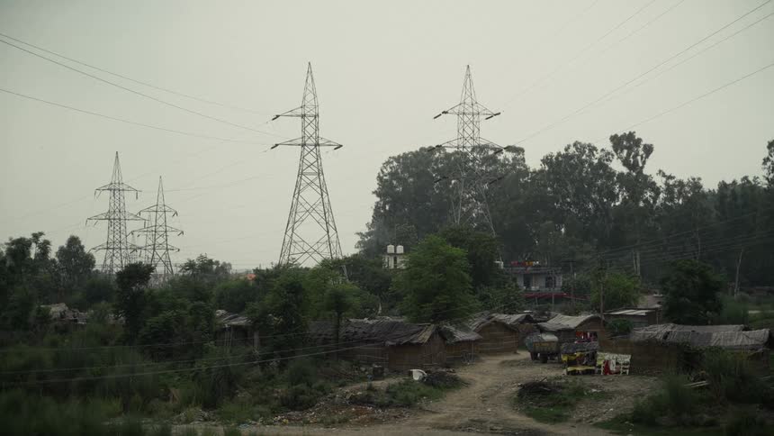 Electric transmission towers crossing village with simple houses dense vegetation and dirt road