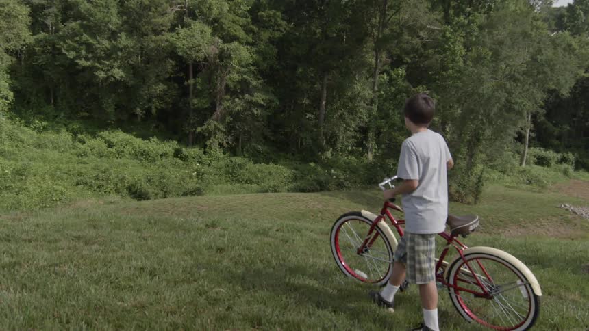 A boy walks his bicycle over the grass