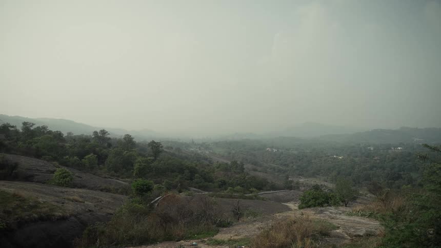 Mountainous landscape with dense vegetation rocky outcrops and scattered white buildings in the distance