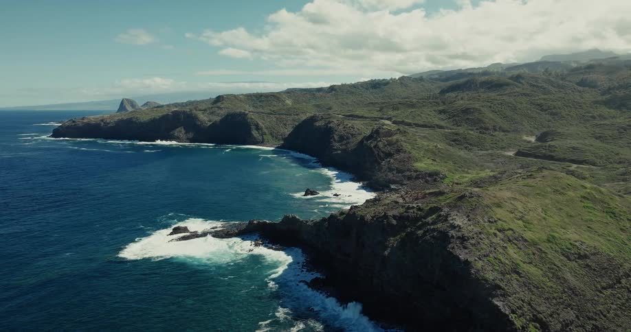 Coastal landscape with green cliffs and rough sea under partly cloudy sky