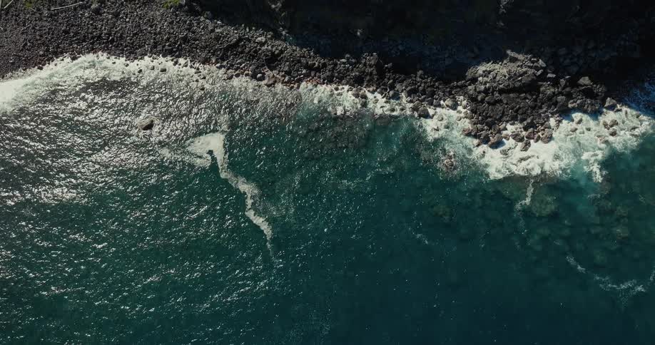 Aerial view of rocky coast with waves crashing on dark rocks and bluegreen sea