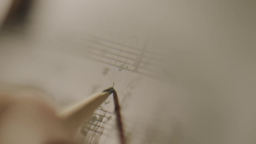 A person writes with a pencil on sheet music
