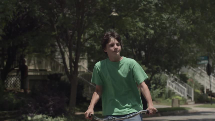 Boy riding a bicycle down a neighborhood street on sunny day