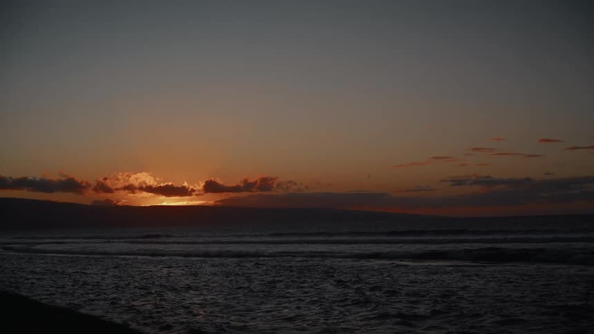 Waves splash and roll into shore as clouds reflect sunlight on the horizon