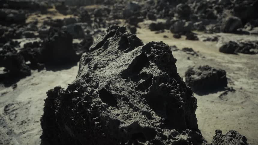 Porous volcanic rock in foreground with arid rocky terrain in background under clear sky