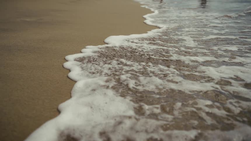 Sea foam spreading over wet sand on a calm beach