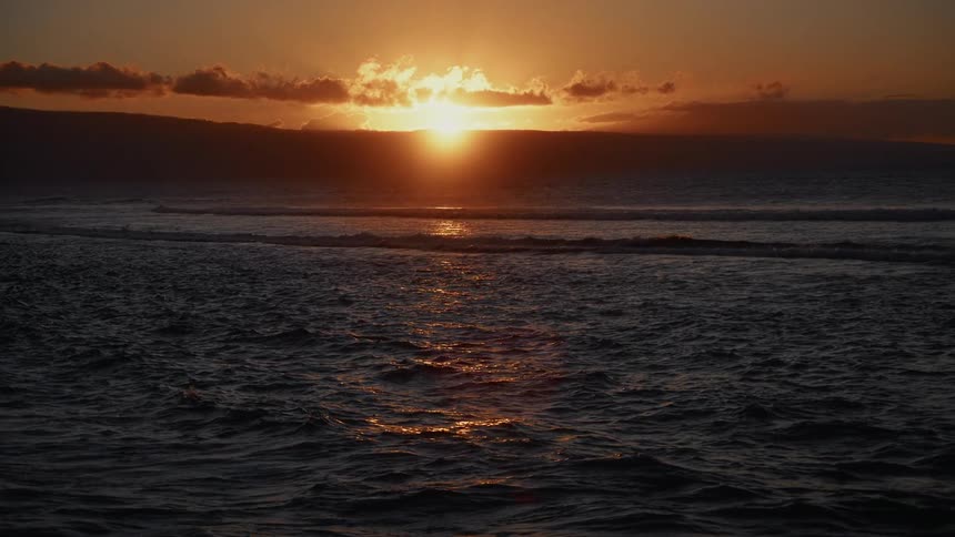 Ocean scene at sunset with sun behind clouds and golden reflections on the water