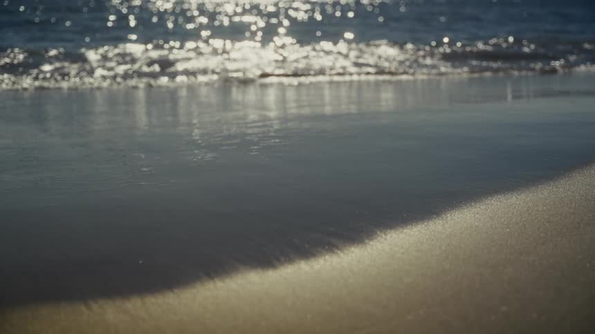 Sea waves and tide with sun reflecting on them next to the beach outdoors during day time