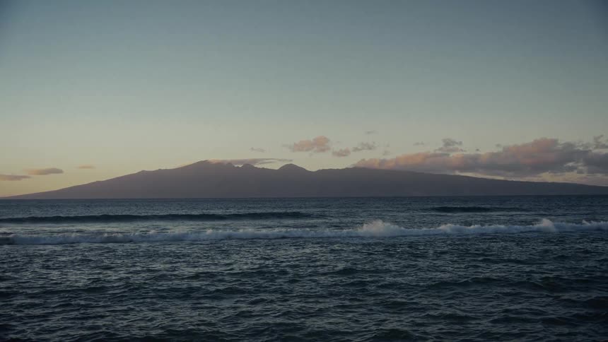A mountain on island at sunrise while waves are breaking at the beach