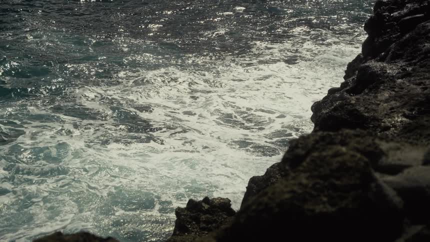 Waves at the sea next to a rocky cliff on the coast outdoors