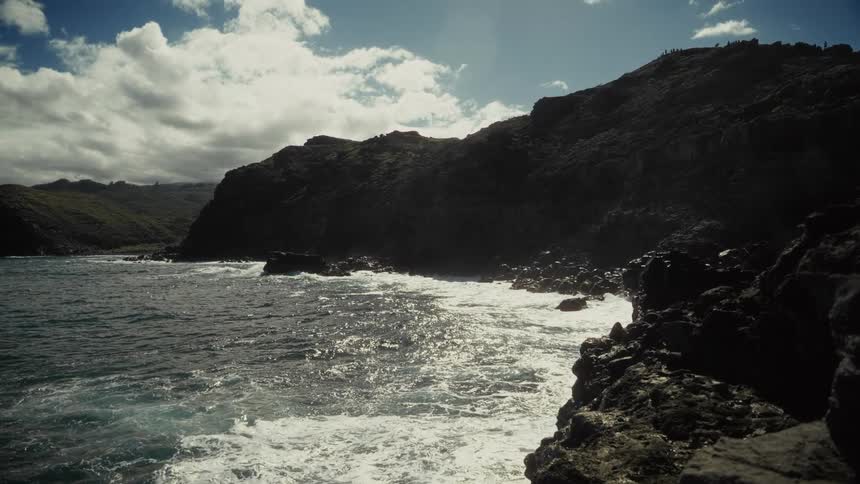 Rocky cliff next to the ocean with green hills on the background outdoors during day time