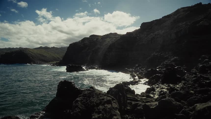 A mountainous coastline stretches along the ocean where waves crash violently against the rocky shoreline