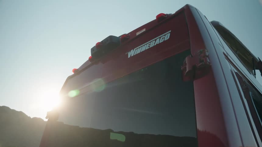 The sun flares brightly behind the top rear of a red winnebago rv