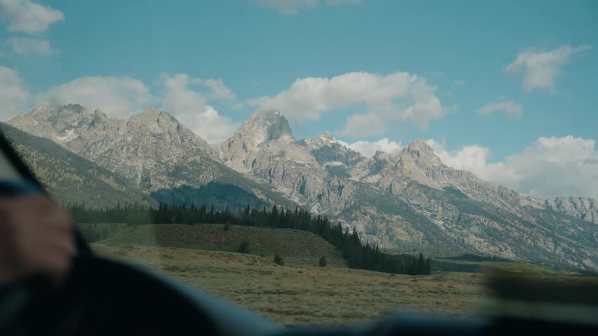 View from inside an automobile traveling across rural land with mountains in the distance