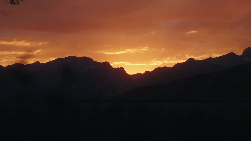 Vibrant sunset behind mountains with orange sky and dark silhouettes in the foreground