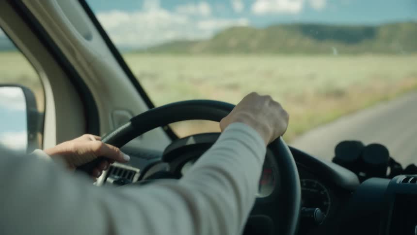 An adult drives a car along a remote road near a mountain range
