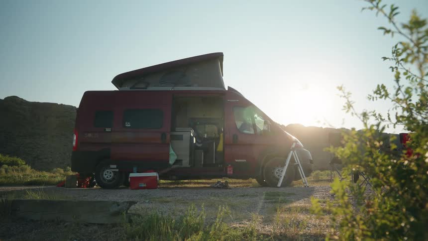 Red camper van with raised roof parked in nature surrounded by camping gear