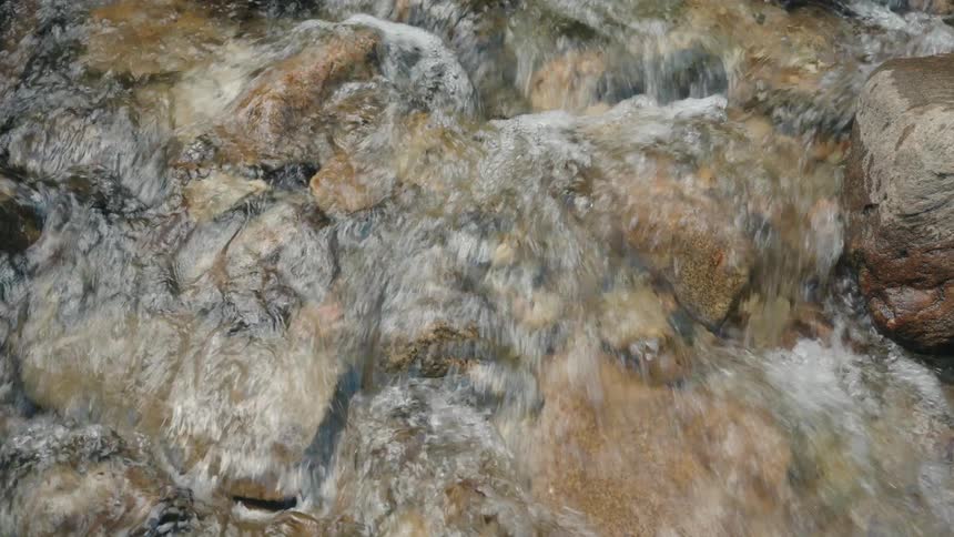 Flowing water moves between rounded stones in a shallow stream