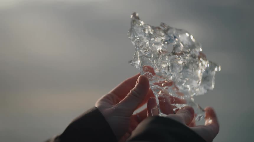 Hands holding translucent ice piece in outdoor setting