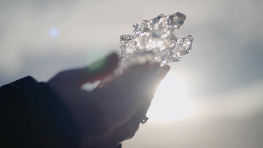 Female hands holding a small piece of melting ice outdoors during day time