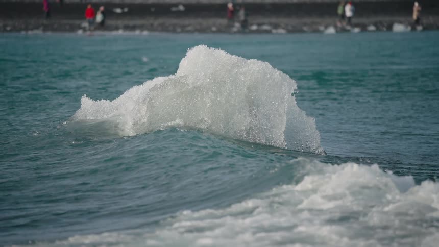 A jagged chunk of ice floats in choppy waves near a shoreline