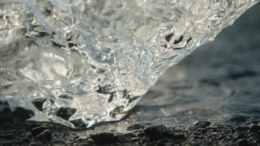 Small glacier fragment forms a translucent block on rocky ground by the waters edge