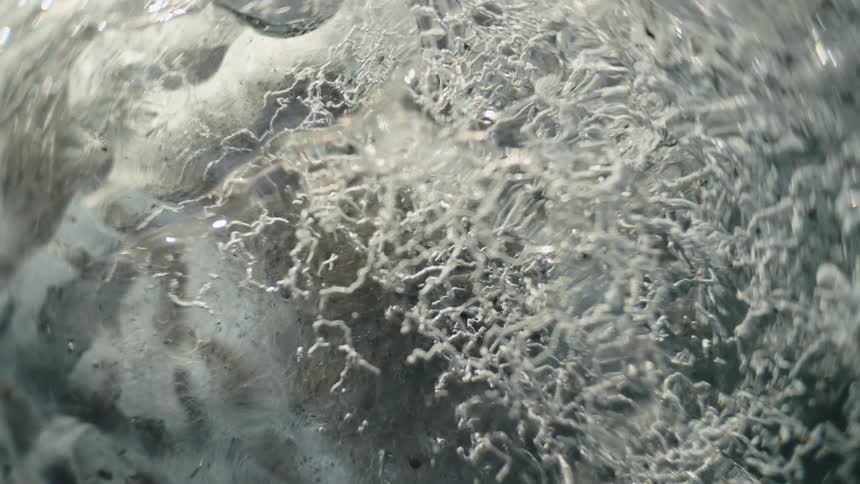 A frozen lake lies still at midday with water visibly flowing beneath the translucent ice