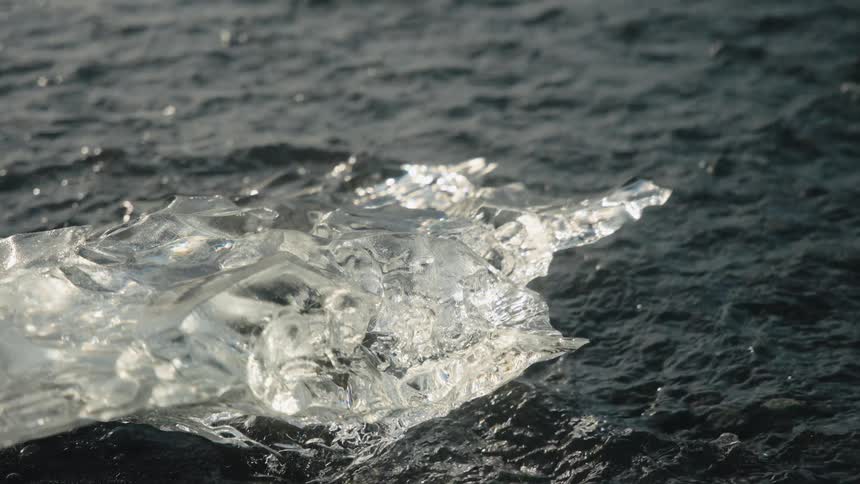 Block of ice on the ground with moving water coming against it outdoors during day time