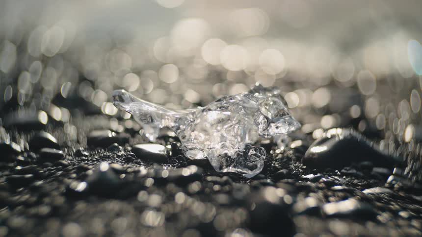 Irregular ice piece on wet pebbles with glowing blurred background