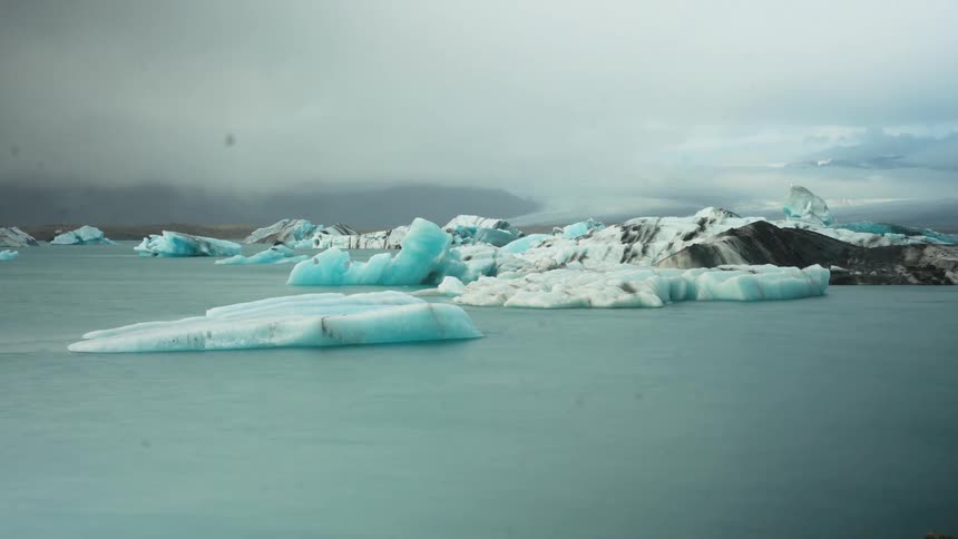 Icebergs floating in still water under overcast sky