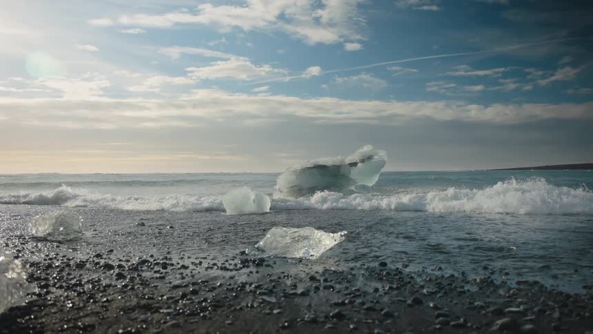 A wave washes upon a coastline with pieces of sea ice on it