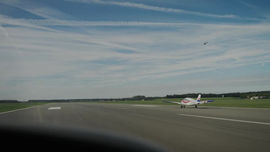 Singleengine plane taxiing on wide runway with helicopter and jet trails in the sky