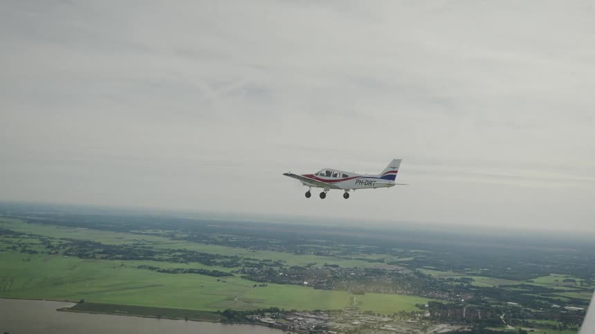 Singleengine aircraft with red white and blue paint flying over green fields and town near water