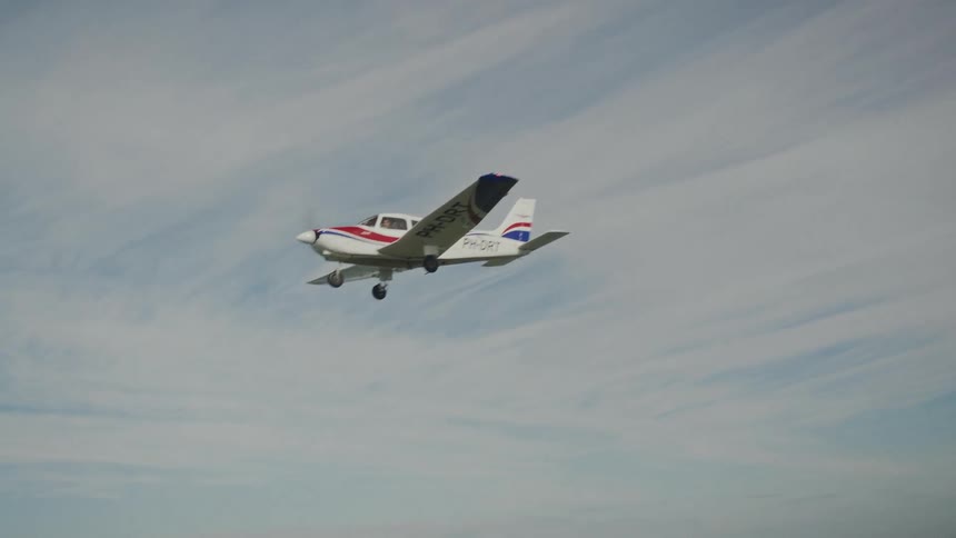 An airplane soars through the midday sky flying over a lake below
