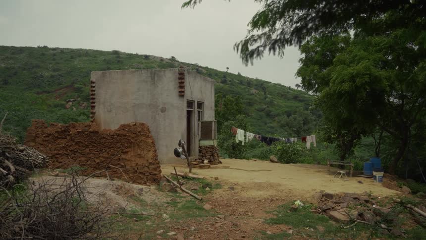 Small rural structure sits amid green hills with laundry hanging in the background
