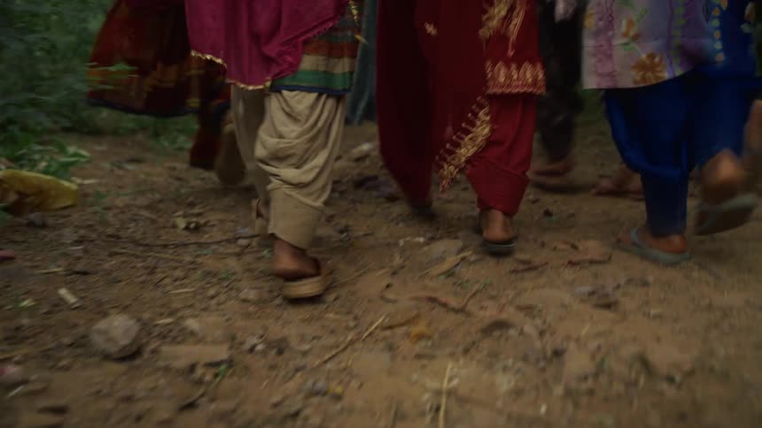 People walk along a dirt path wearing sandals and traditional clothing
